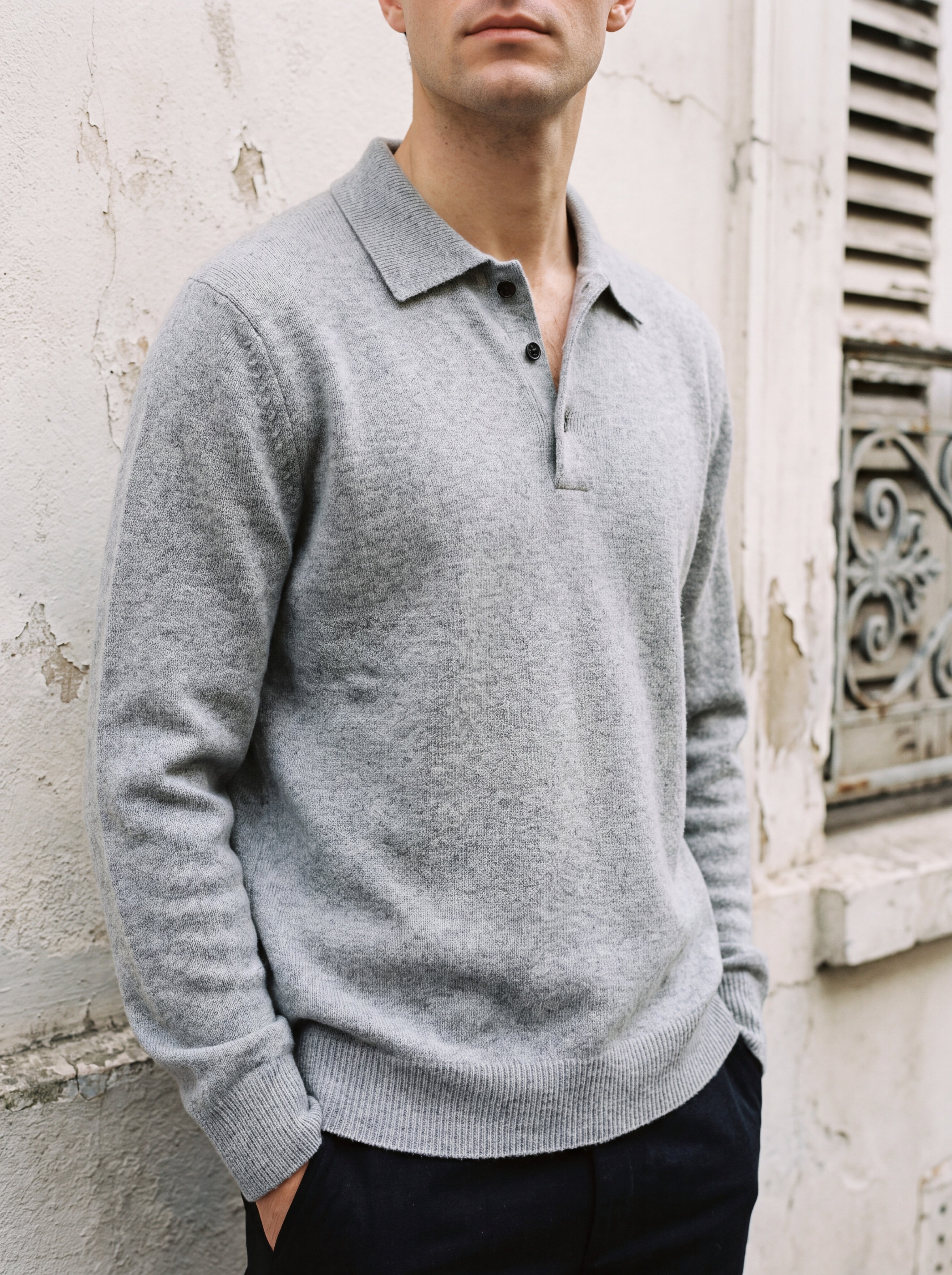 Francesco Bellani Brera cashmere polo worn with the collar open, against a weathered pale plaster wall