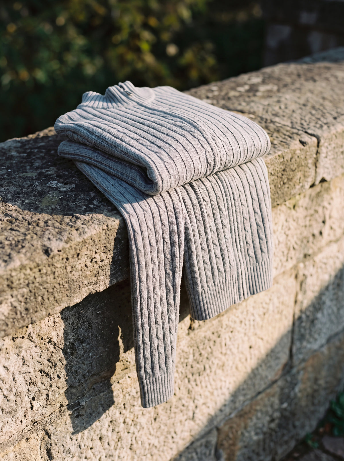 Francesco Bellani Aosta cable-knit wool zip-through folded across a stone ledge, cable pattern visible
