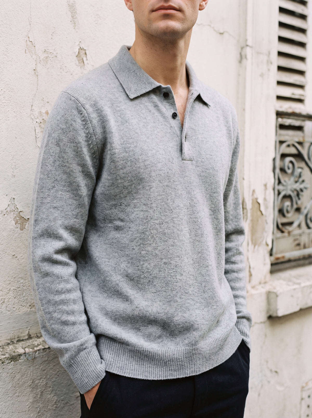 Francesco Bellani Brera cashmere polo worn with the collar open, against a weathered pale plaster wall