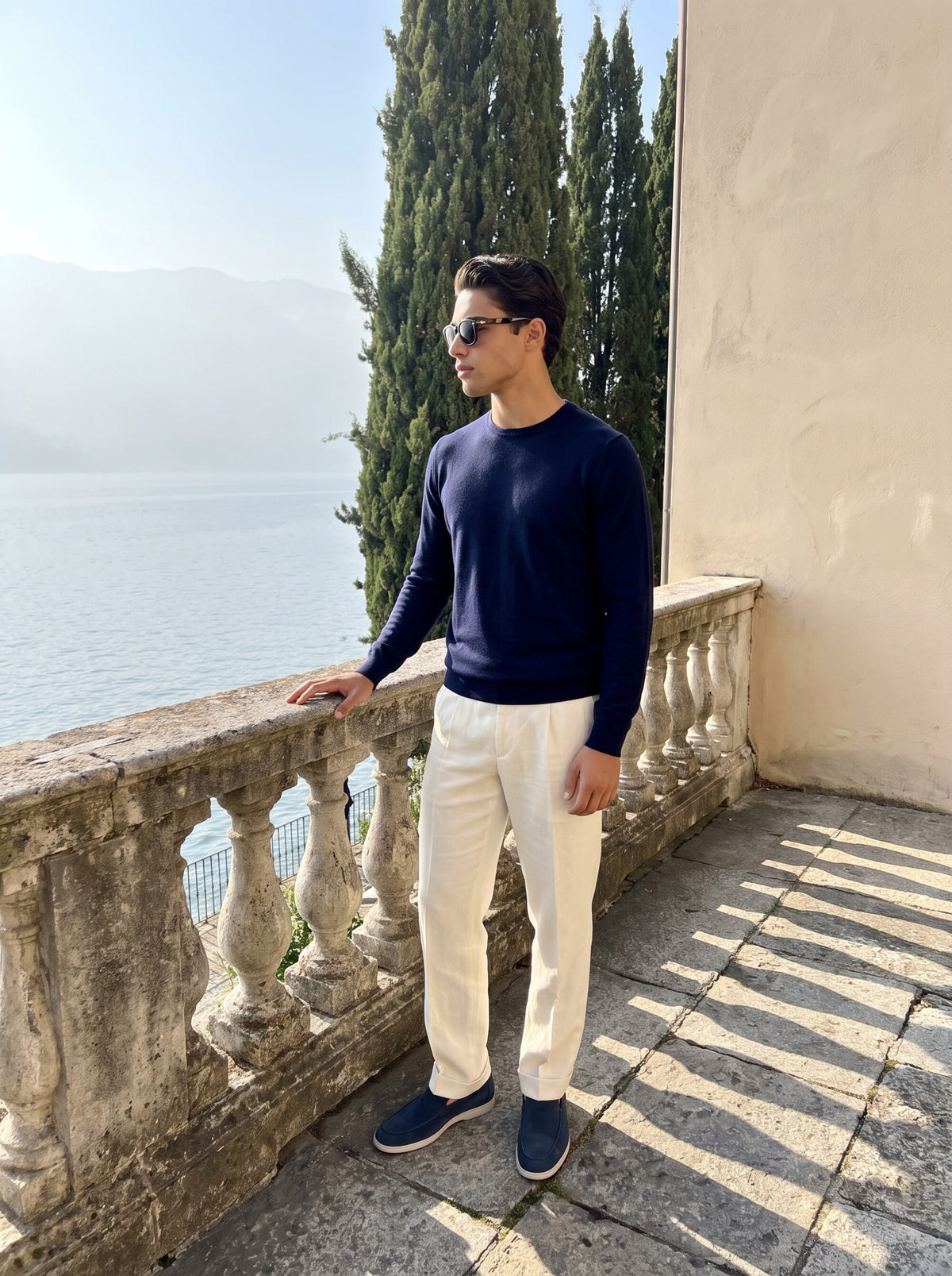 Navy merino pullover and cream linen trousers on a stone terrace above the lake
