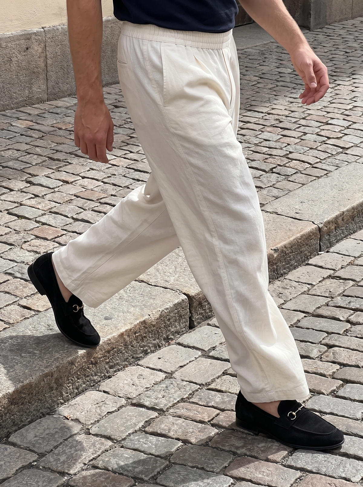 Natural linen trousers in movement across cobbles, showing the drape and single break — Francesco Bellani Portofino