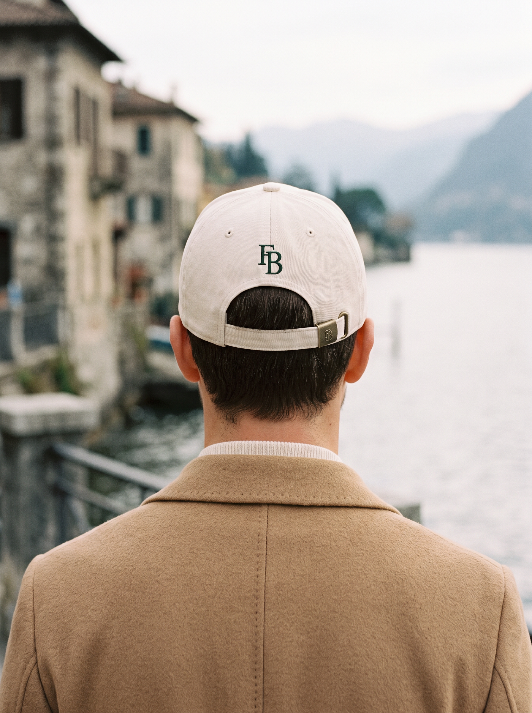 Back of the Rapallo cap showing the FB monogram and engraved brass adjuster, worn with a camel overcoat