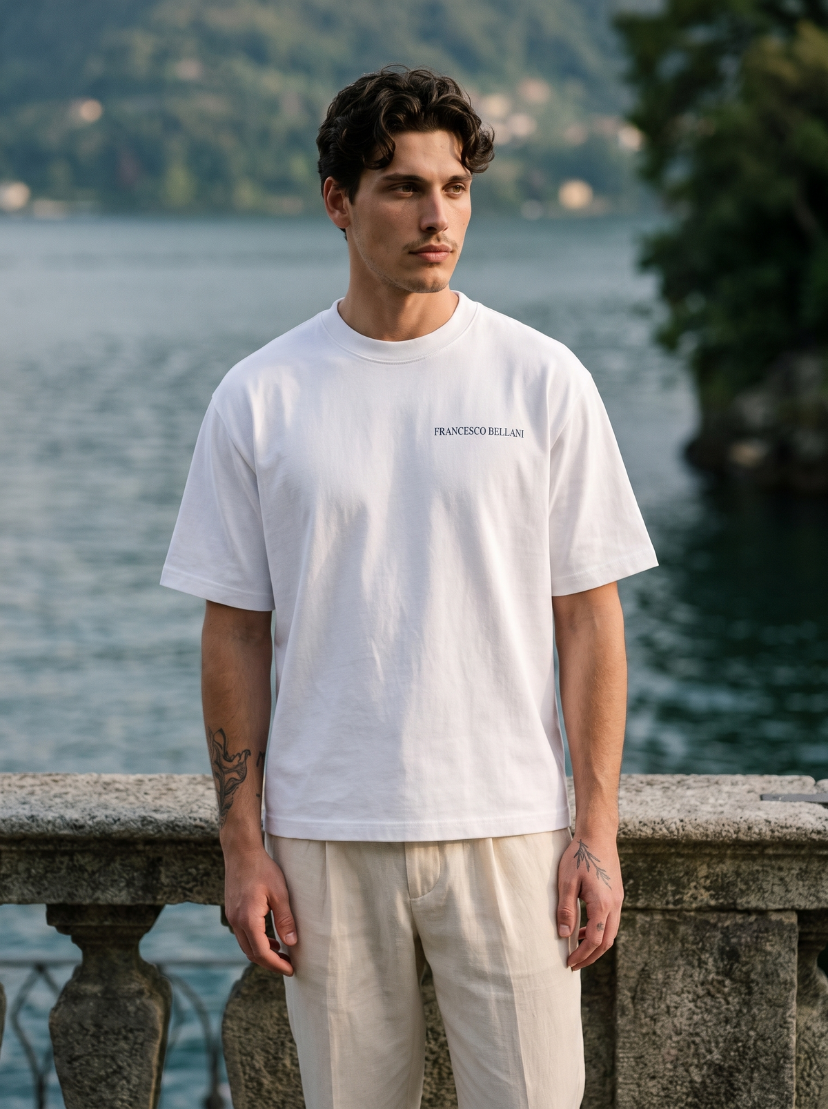 Man wearing the Tremezzo Printed Tee with cream pleated trousers on a terrace above Lake Como