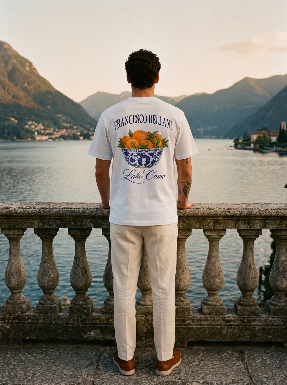 Man wearing the Tremezzo Printed Tee at a stone balustrade above Lake Como, back view showing the full print