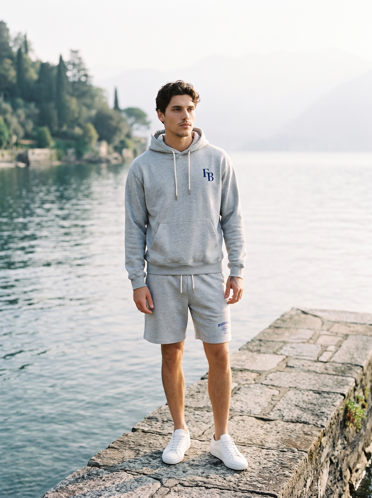 Man wearing the grey marl Moltrasio Printed Hoodie and matching Laglio Jersey Short on a jetty on Lake Como